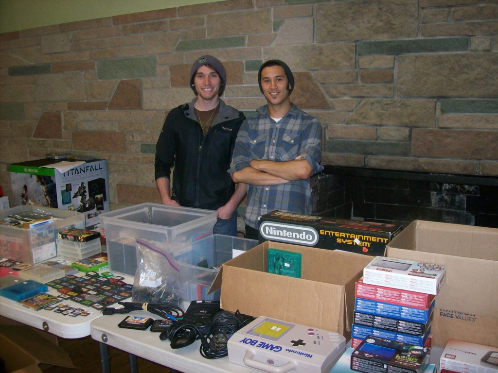 shot of two young men in stocking caps in front of tables filled with video games and cargridges