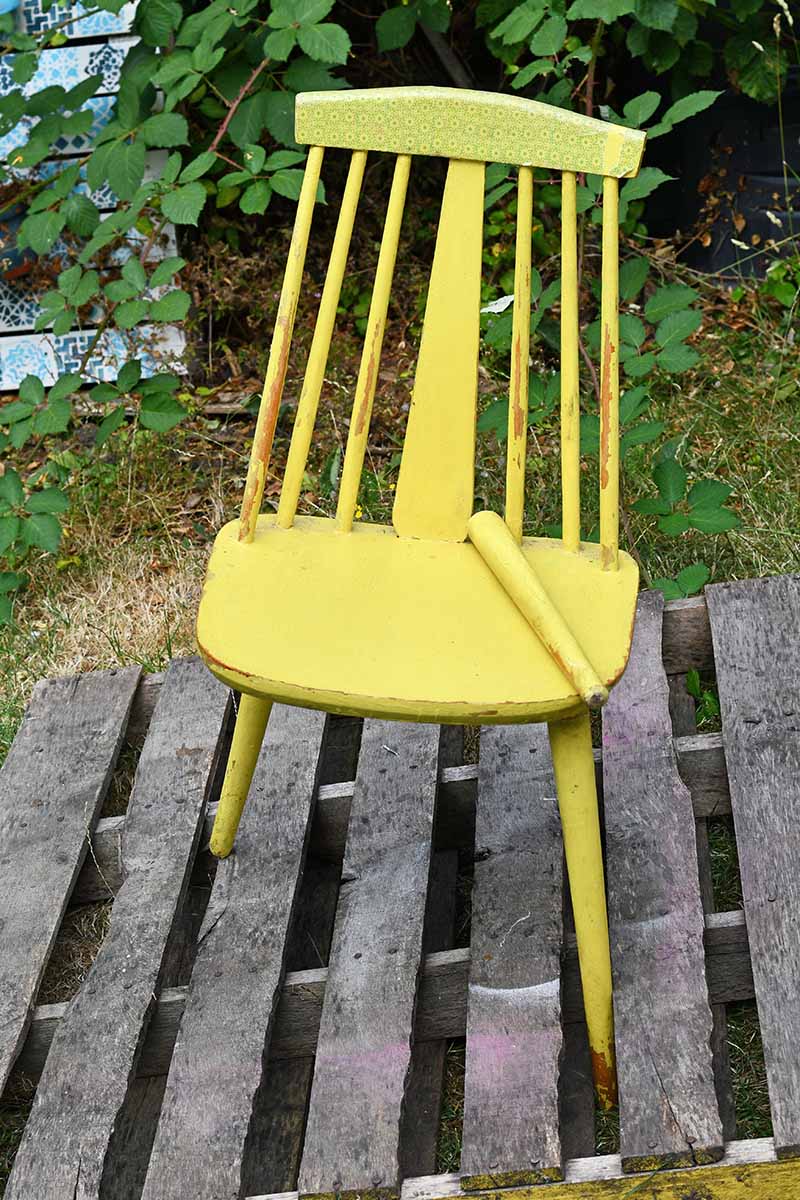 A wooden yellow chair missing a leg.