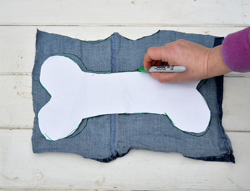 A hand hold the white stencil of a dog bone on top of a stack of denim. 