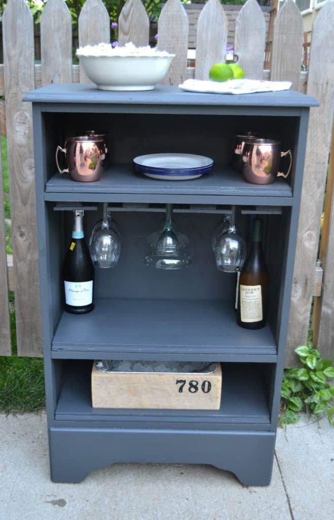 A small, blue home bar with plates, cups and wine bottles.
