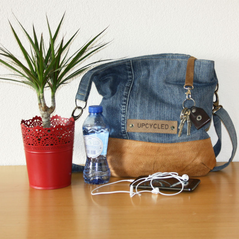 A denim bag with a leather bottom sits on a table with a plant and headphones.