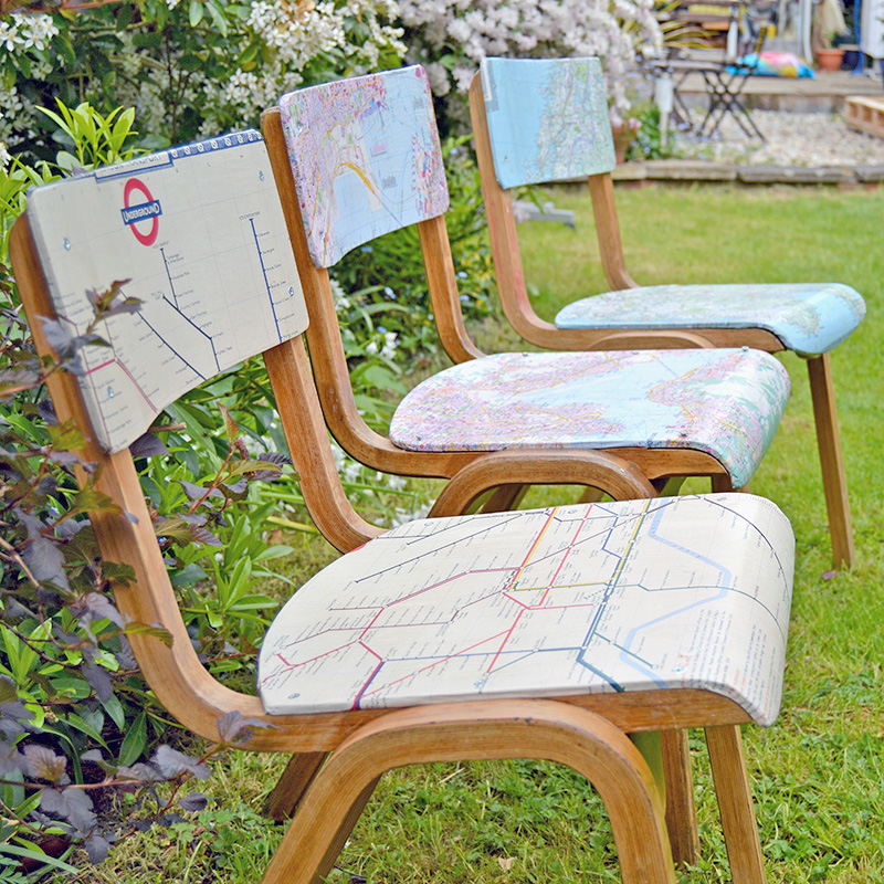 Three chairs, decoupaged with maps, sit on a lawn. 