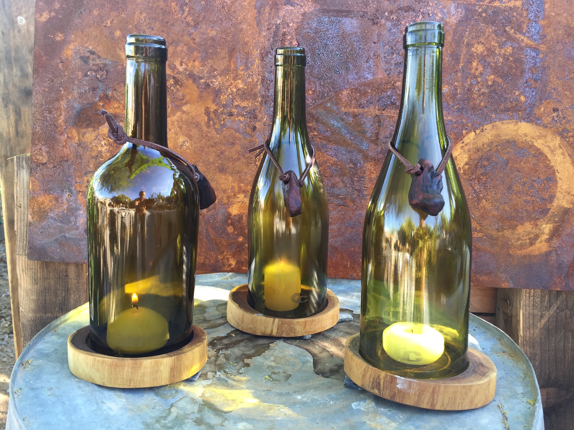 Three candles sit inside three wine bottles, each sitting on a wood coaster.