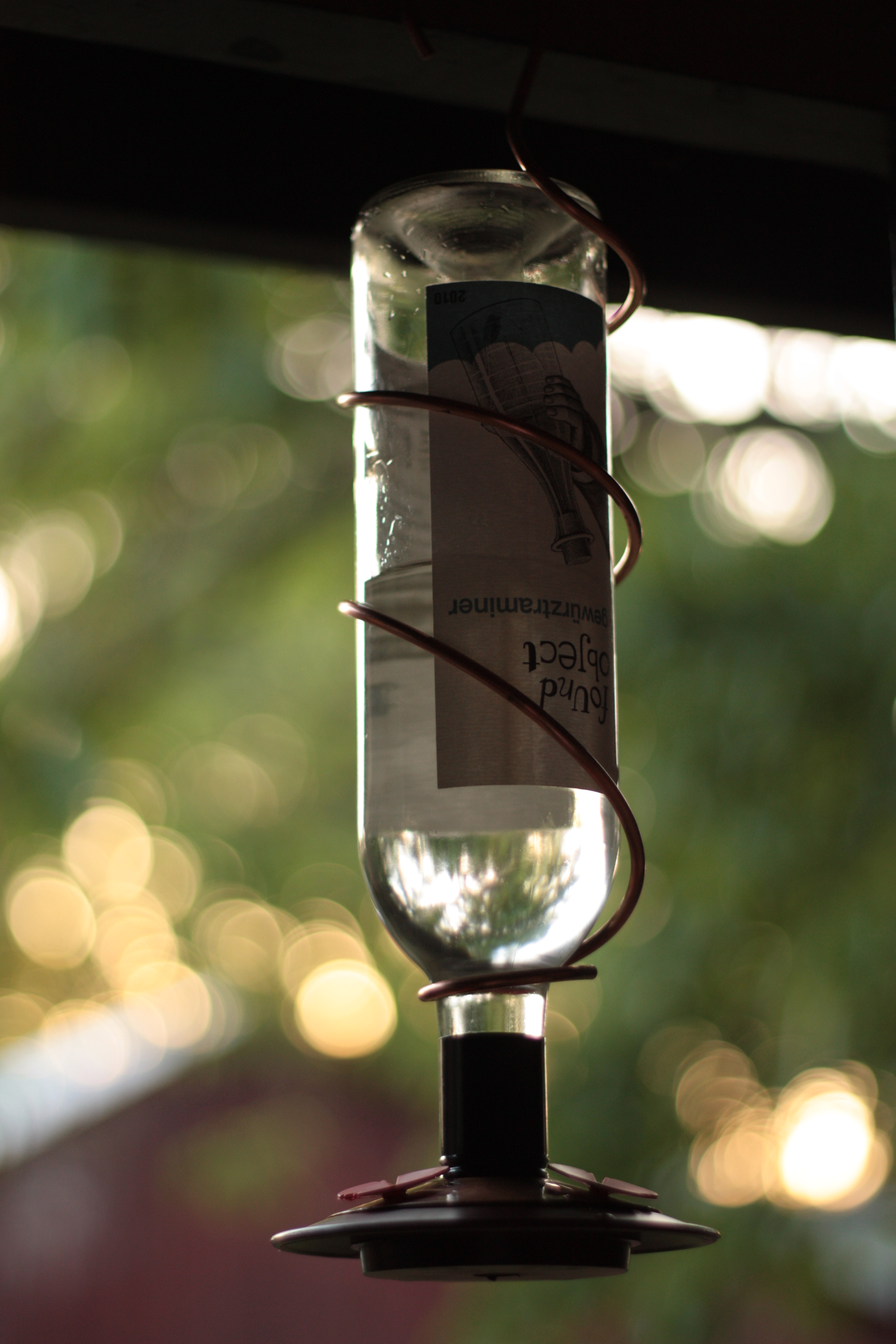 A wine bottle upcycled into a bird feeder hangs from a porch eave.