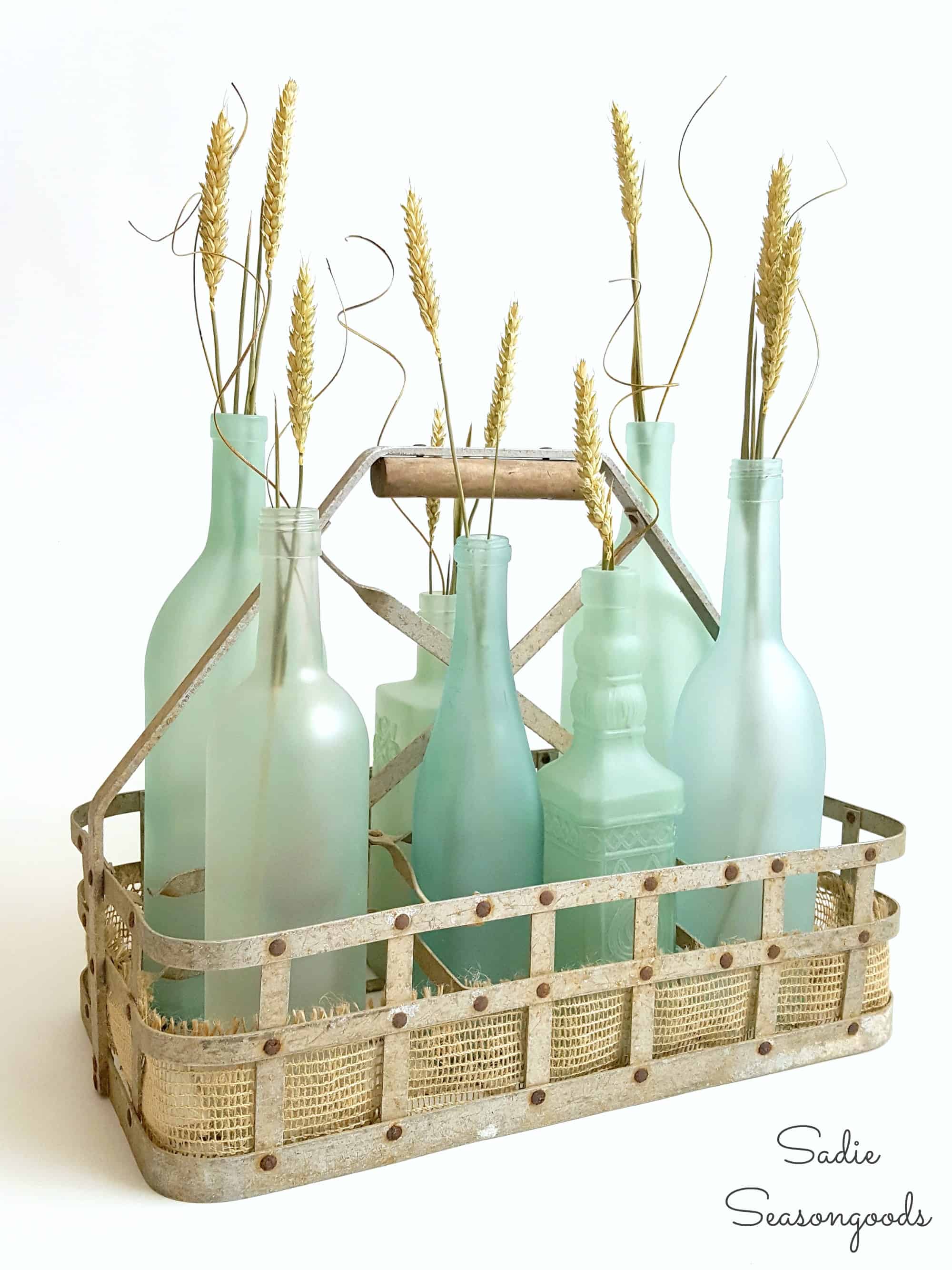 Sea glass-colored vases filled with dune grass sit in a brown basket.
