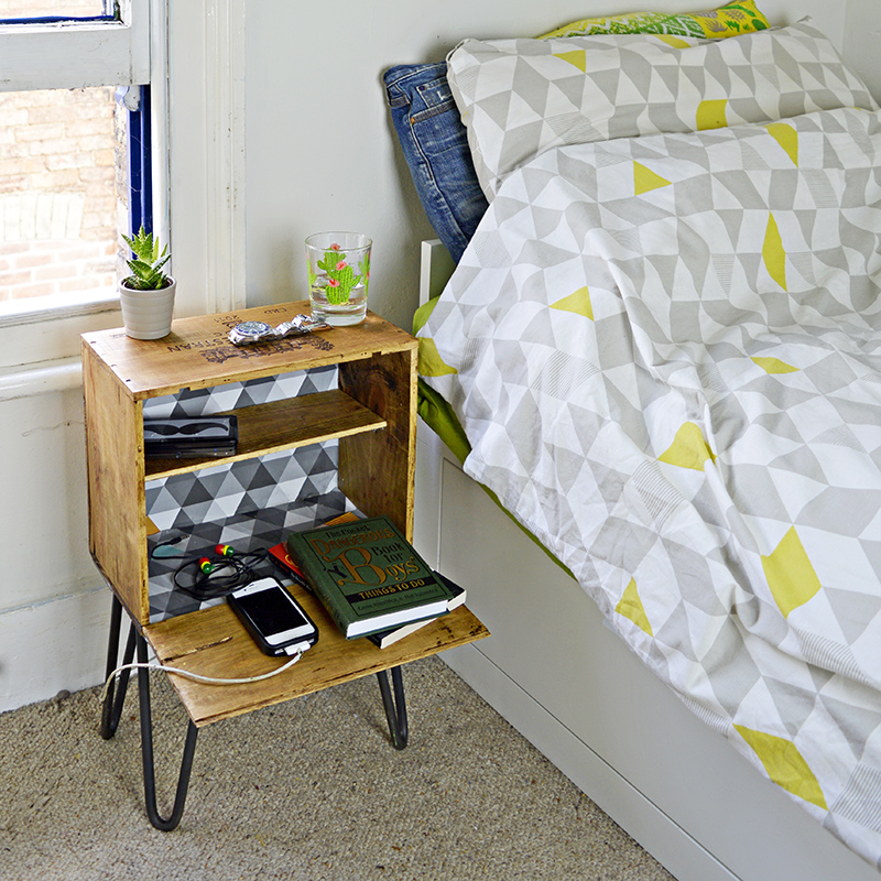A wine crate night stand sits next to a bed with a yellow and gray comforter.
