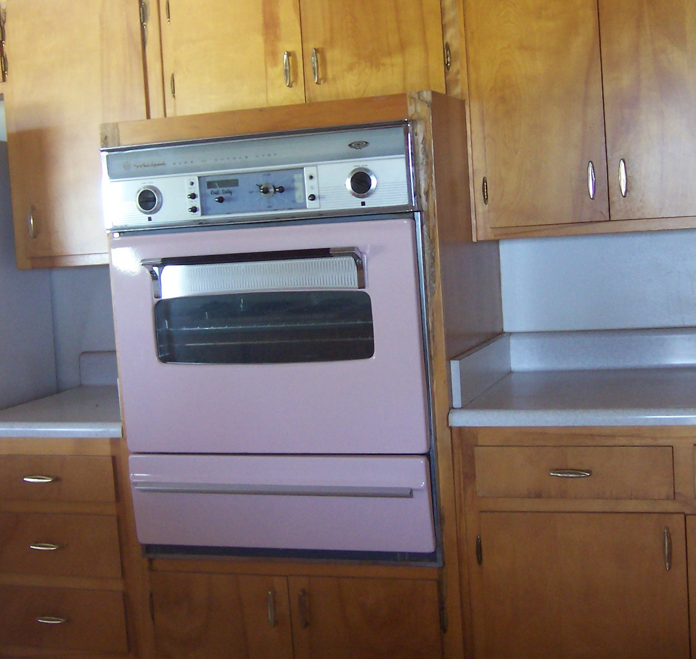 A pink wall oven in a wooden kitchen.