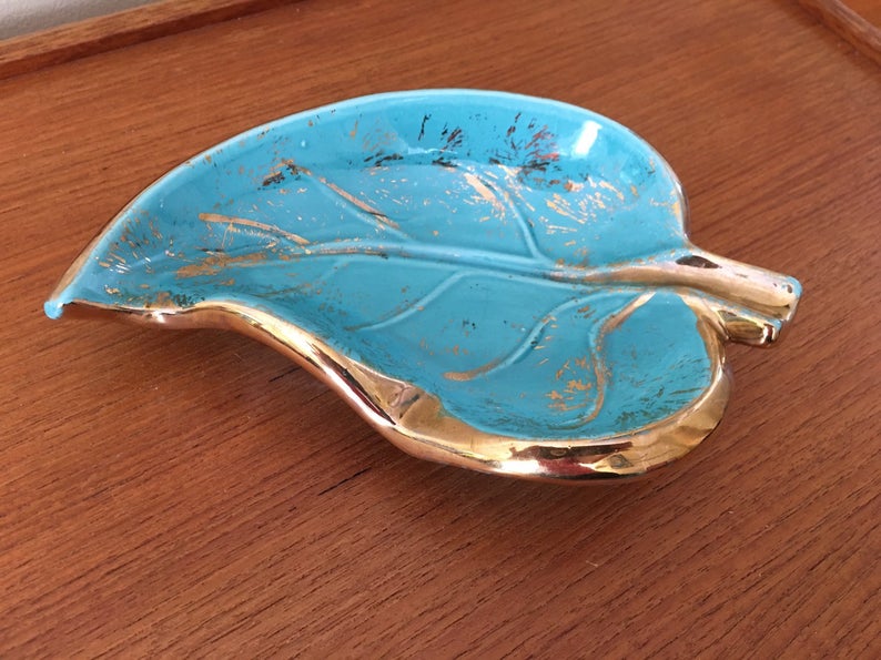 Blue and gold ashtray shaped like a leaf sitting on a wooden surface.