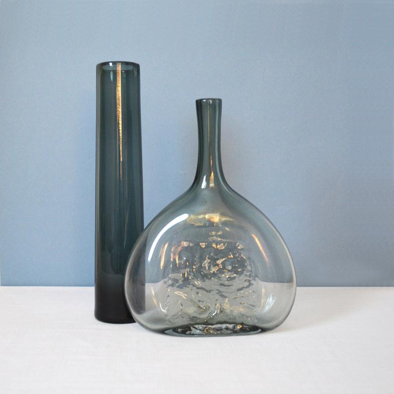 Two gray glass vases on a white counter with blue background.