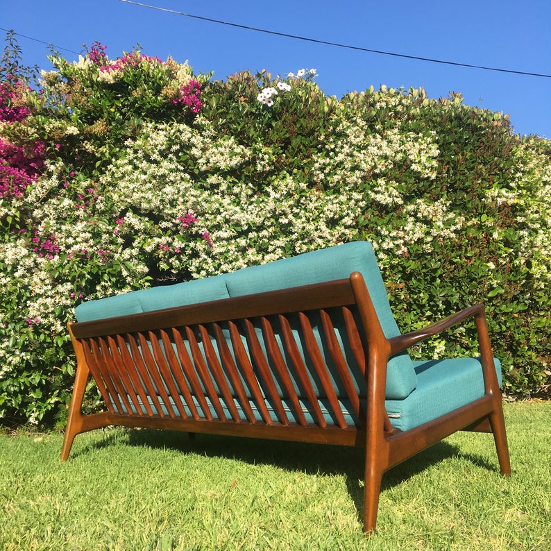 Back of wooden sofa with teal upholstery in a garden.